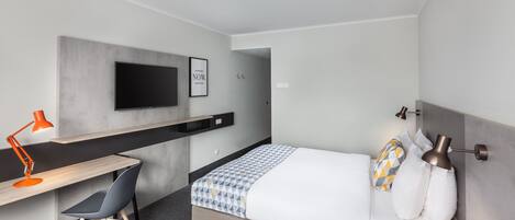 Una habitación de hotel moderna con una cama, un escritorio, una silla, un televisor y una lámpara de noche.