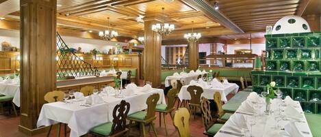 A restaurant with multiple tables set for dining, wooden beams on the ceiling, and a green patterned wall in the background.