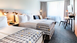 A hotel room with two beds, a desk, a chair, and a large window with curtains. - Holiday Inn Munich - South by IHG (Munich)