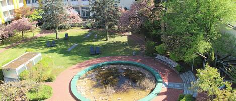 Una fuente circular rodeada por un sendero de ladrillos, con árboles y un edificio al fondo.