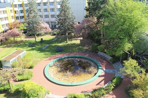 A circular water feature surrounded by a brick walkway, with trees and a building in the background. - Holiday Inn Munich - South by IHG (Munich)