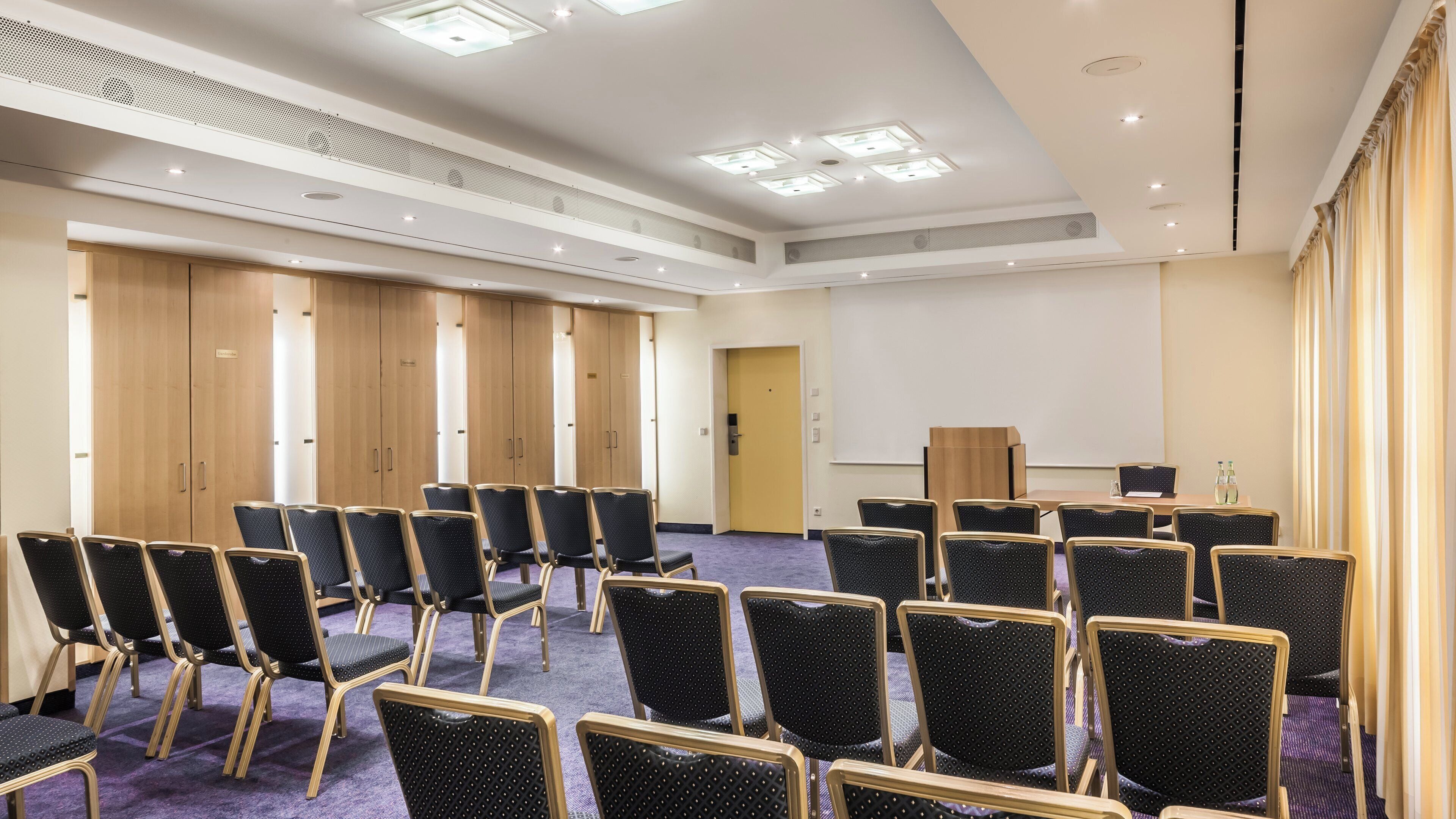 A conference room with rows of chairs, a podium, and a large screen.