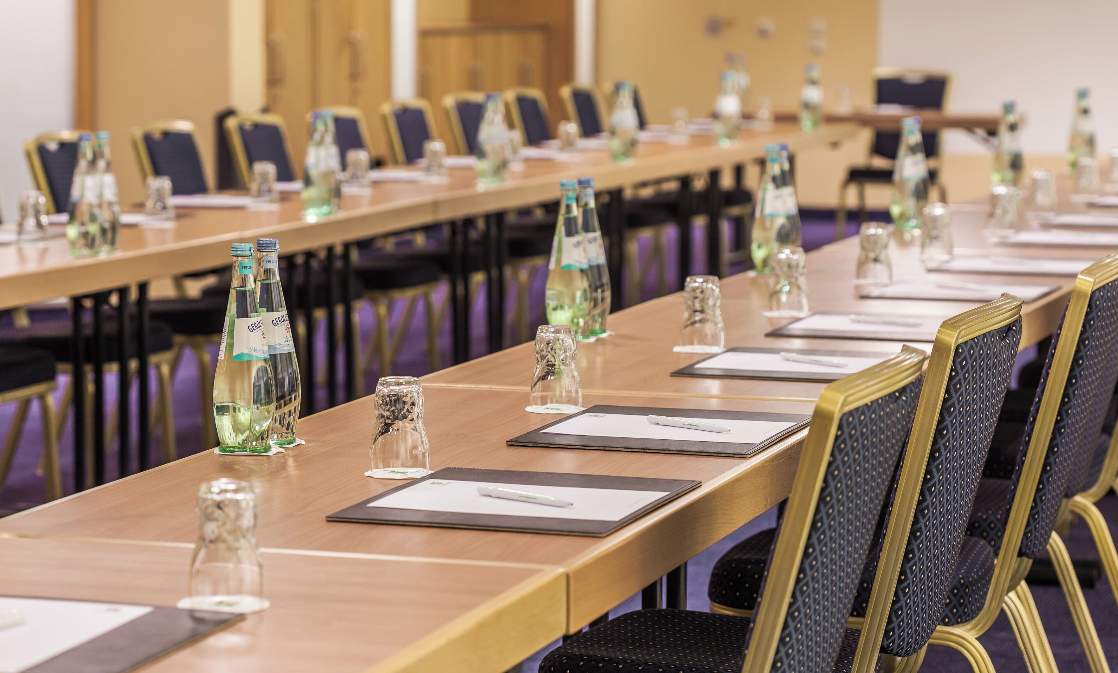 A conference room with long tables, chairs, water bottles, and documents.