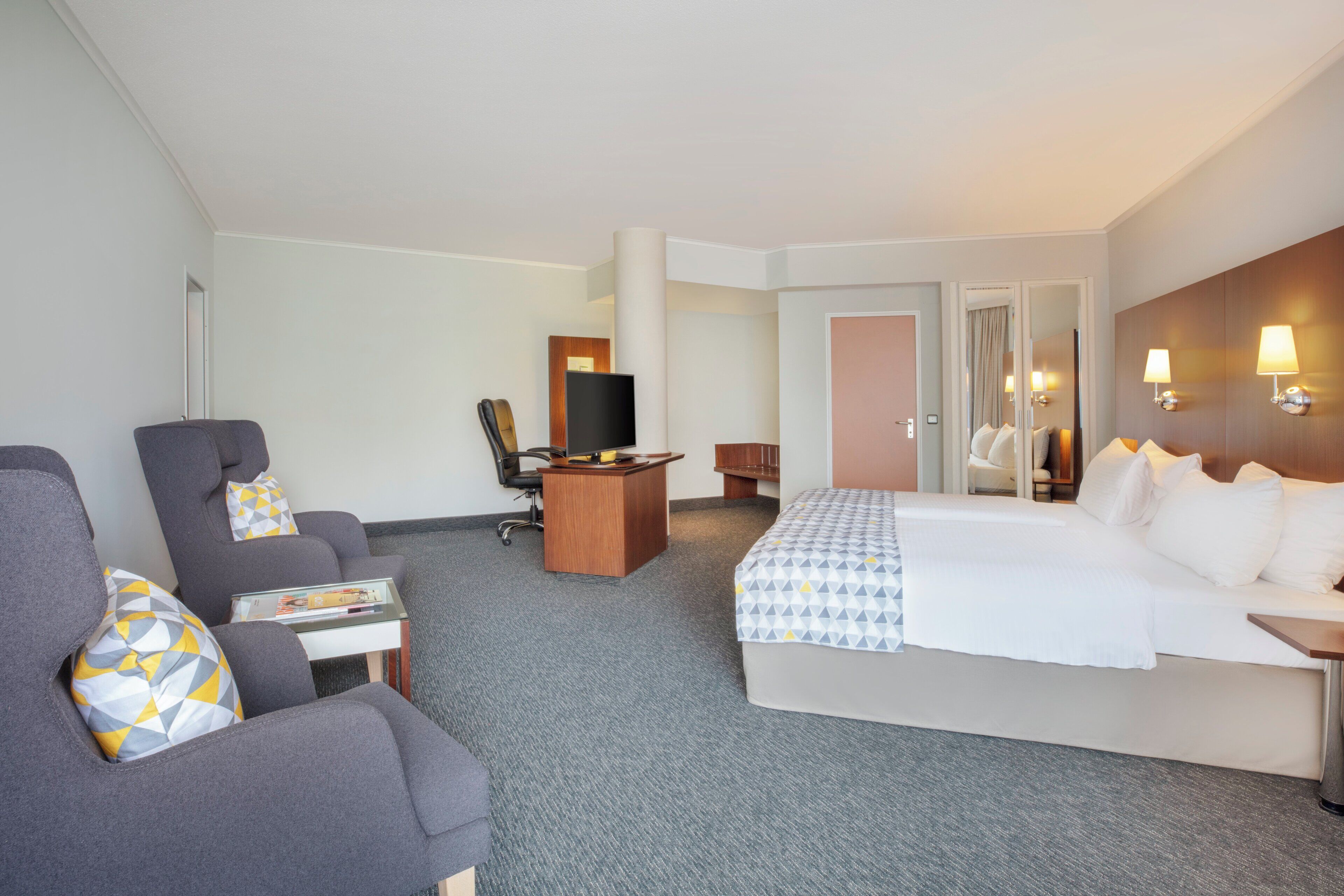 Une chambre d’hôtel avec un lit, un bureau, une chaise et un téléviseur.