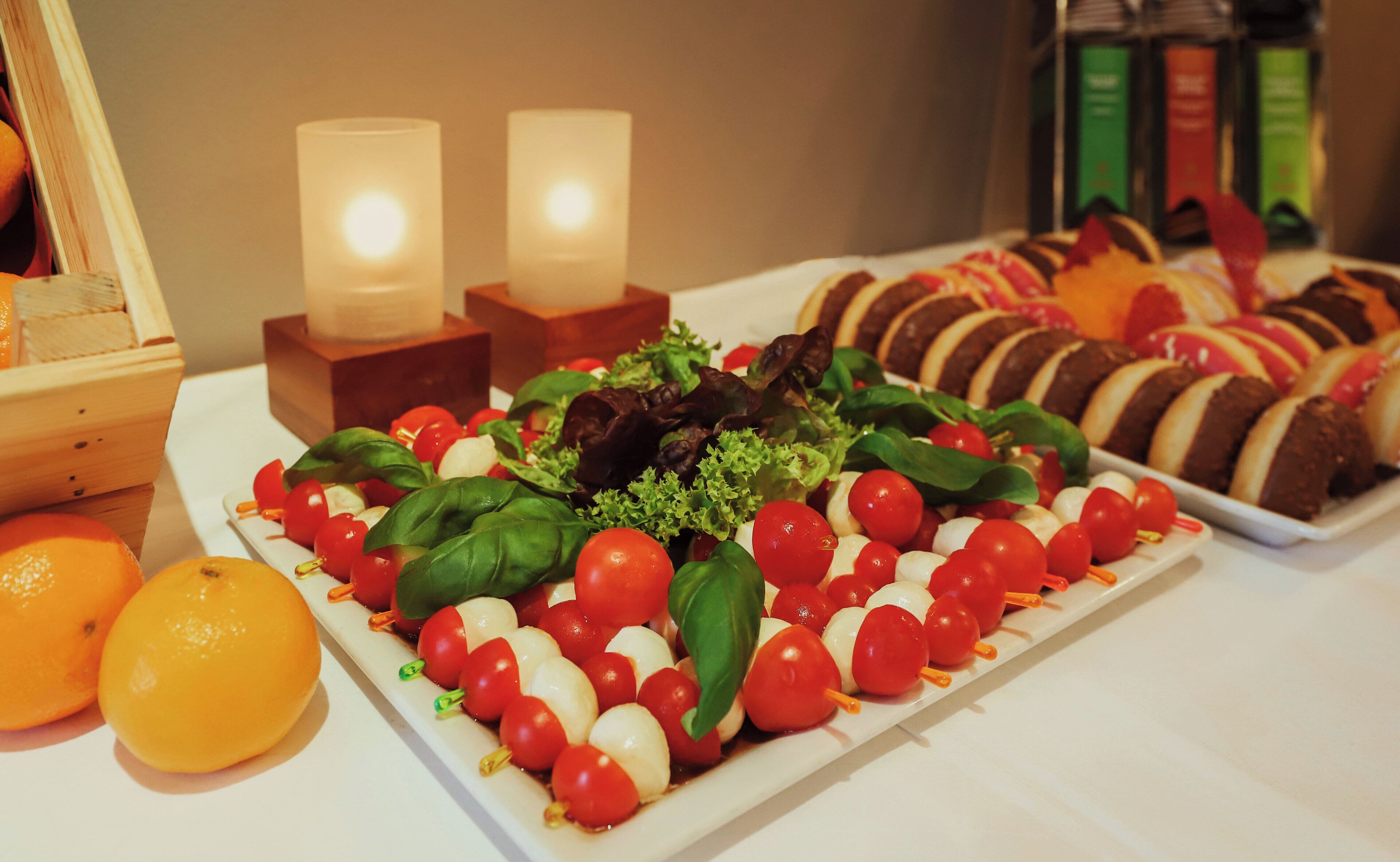 A table with a variety of food items, including a plate of cherry tomatoes and mozzarella, and a tray of bread with chocolate and fruit.