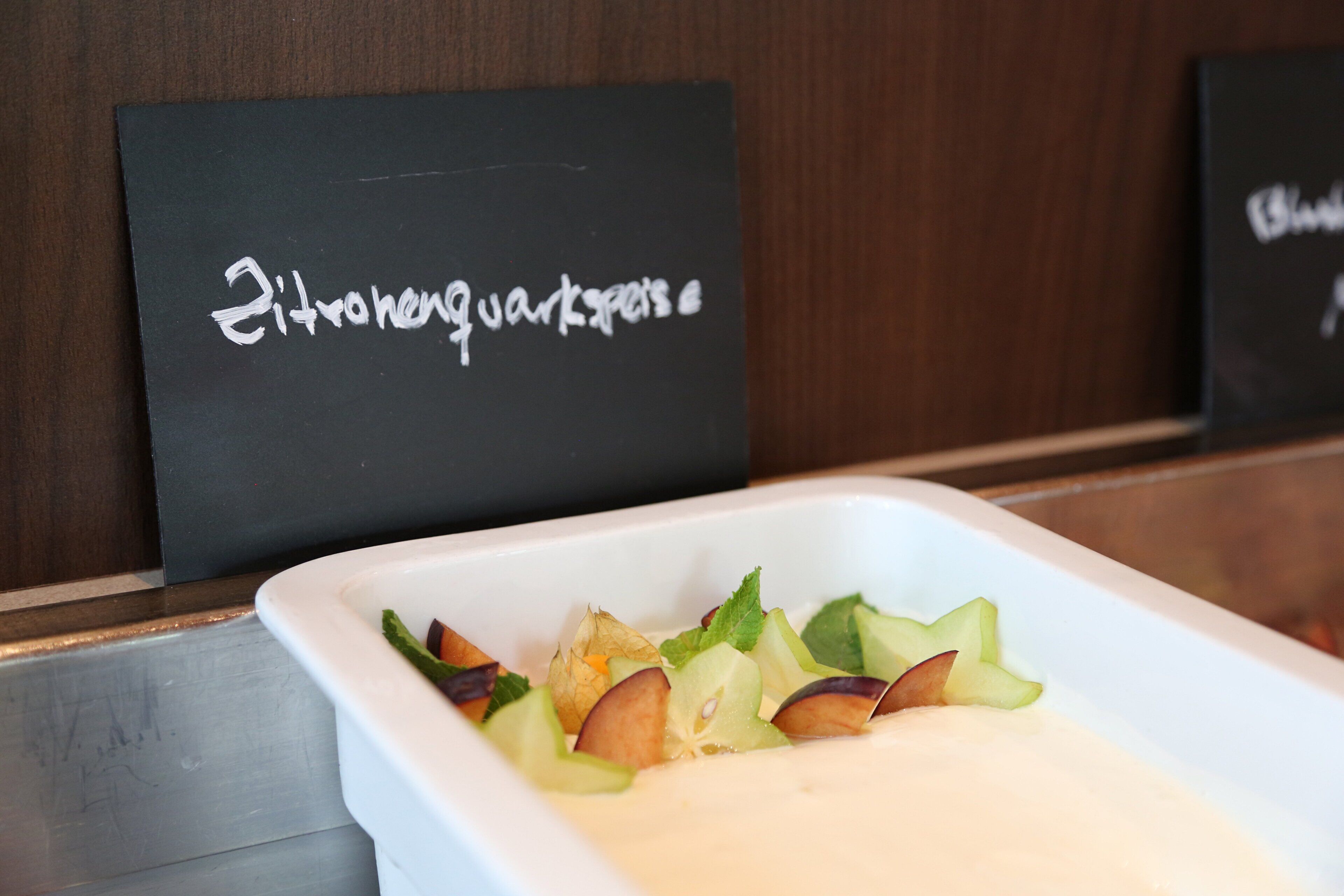 A white rectangular dish with a salad on a table, with two black signs in the background.