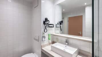 Une salle de bain moderne avec des carreaux blancs, un lavabo, un miroir et deux sèche-cheveux fixés au mur.