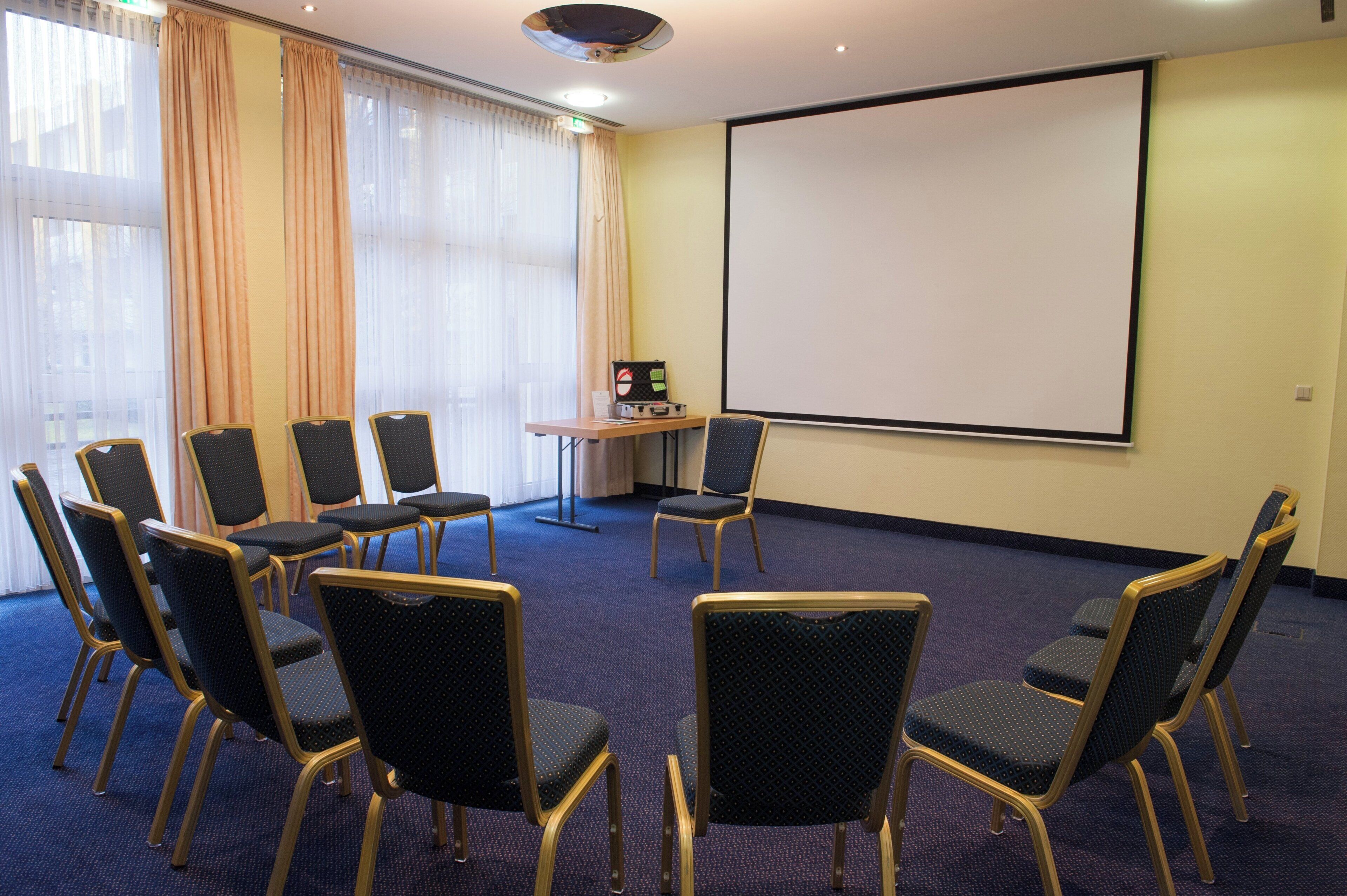 A conference room with a projector screen, a table with a laptop, and several chairs arranged for a meeting.