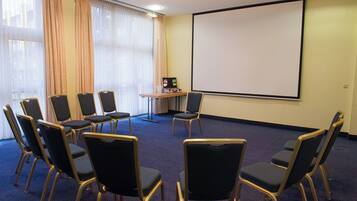 A conference room with a projector screen, a table with a laptop, and several chairs arranged for a meeting.