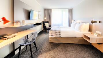 Een hotelkamer met een bed, bureau, stoel en een televisie aan de muur.