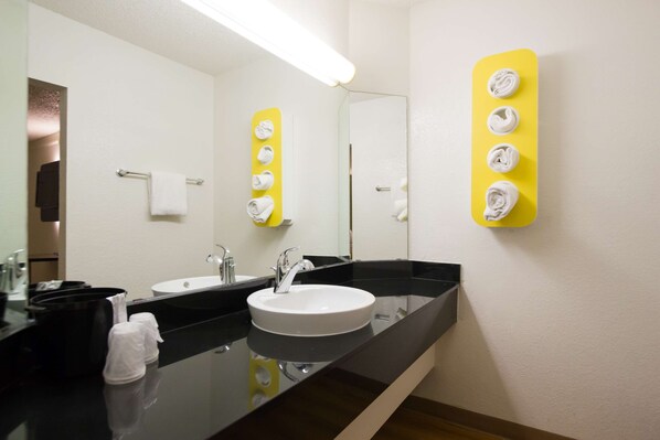 A modern bathroom with a black countertop, a white sink, and a mirror. There are two towel dispensers on the wall, one yellow and one white. - Motel 6 Austin, TX - Midtown (Austin)
