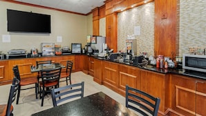 A kitchen with wooden cabinets, a black countertop, and a microwave. There is a table and chairs set up for dining.