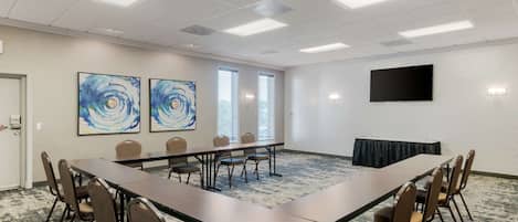 A conference room with a long table, chairs, artwork on the walls, windows, and a flat-screen TV.