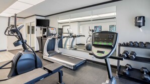 A gym with treadmills, an elliptical, and dumbbells on shelves.