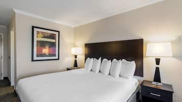 A hotel room with a large bed, two bedside tables with lamps, a framed picture on the wall, and a dark headboard.
