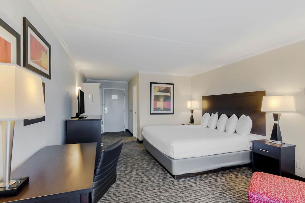 A hotel room with a large bed, a desk, a chair, and a small table.