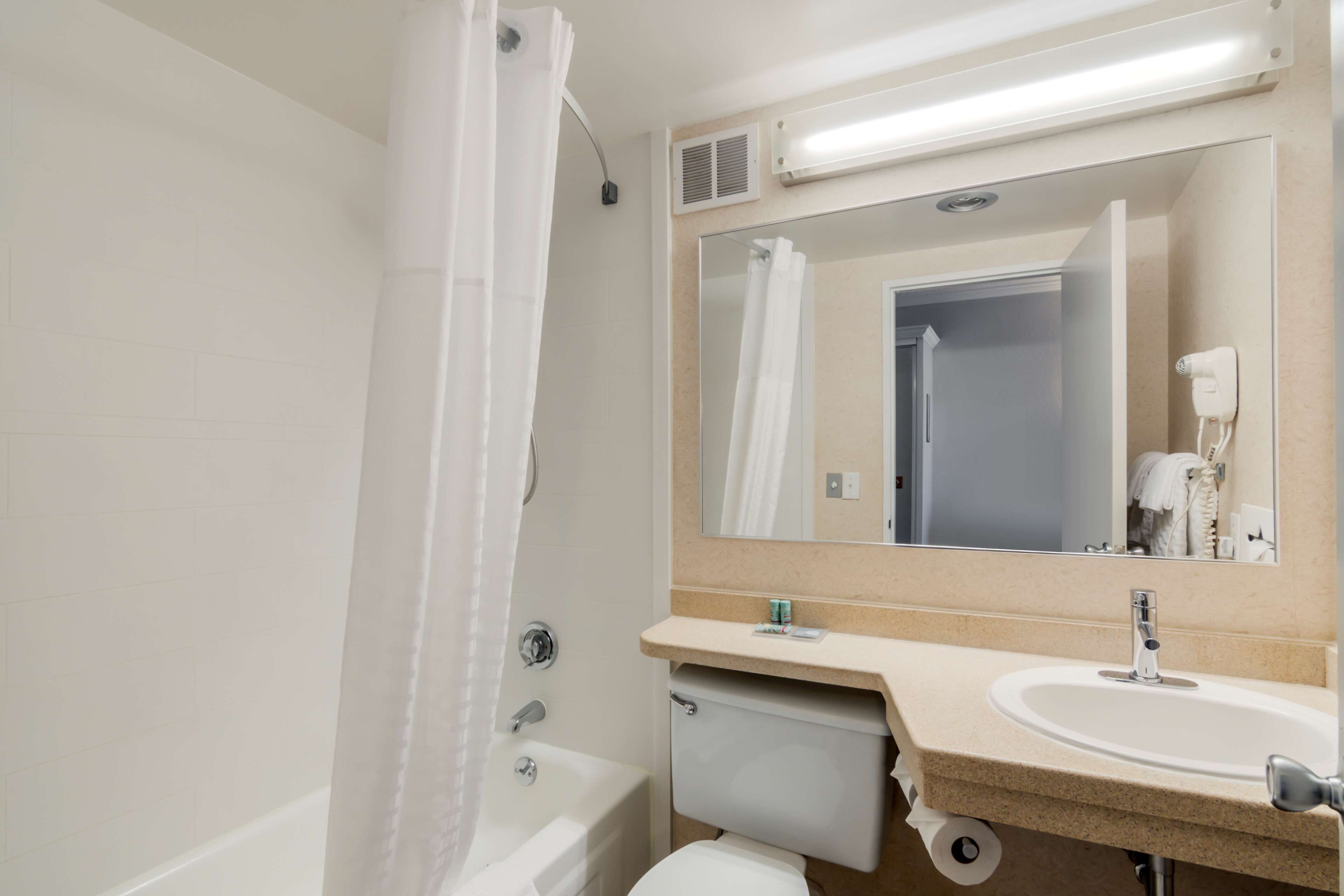 Un baño con bañera, inodoro, lavamanos y espejo.