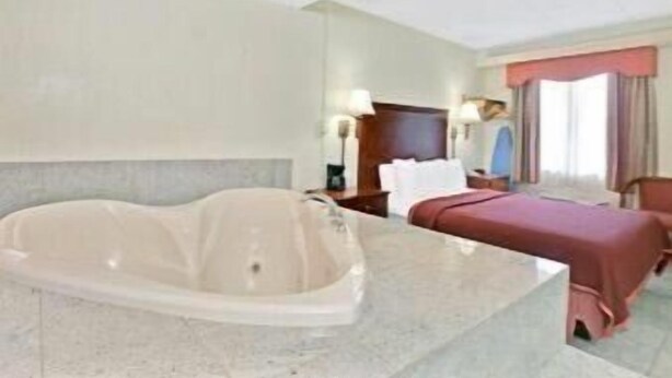 A hotel room with a large bathtub, a bed, a desk, and a window with curtains. - Travelodge by Wyndham Parsippany (Parsippany)