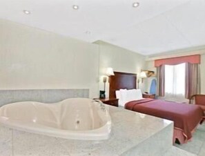 A hotel room with a large bathtub, a bed, a desk, and a window with curtains. - Travelodge by Wyndham Parsippany (Parsippany)