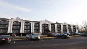 A multi-story hotel with a symmetrical facade, multiple balconies, and a parking lot with several cars. - Travelodge by Wyndham Parsippany (Parsippany)