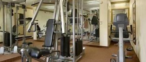A gym with various exercise machines, mirrors, and weights.