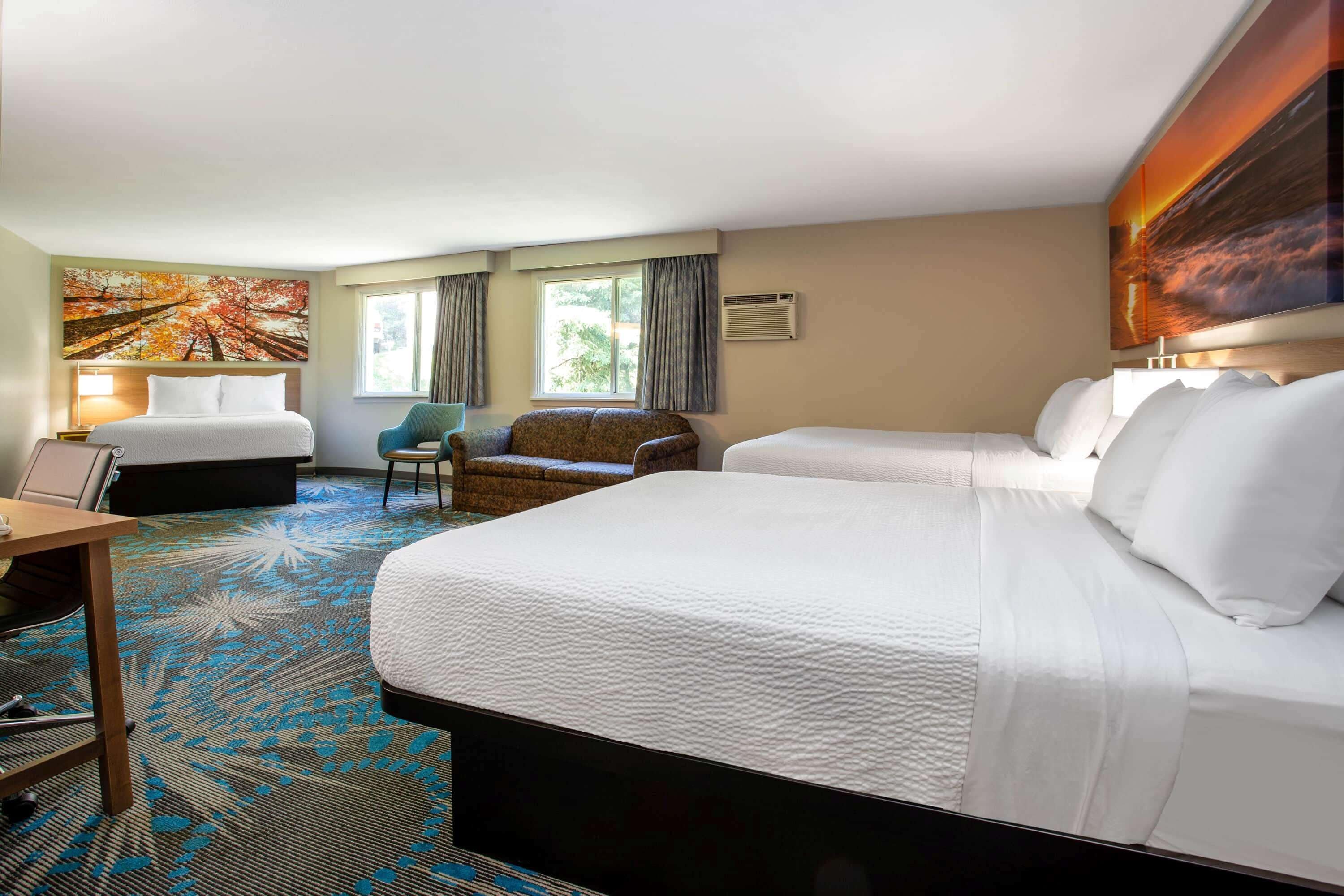 A hotel room with two beds, a desk, a chair, and a large window.