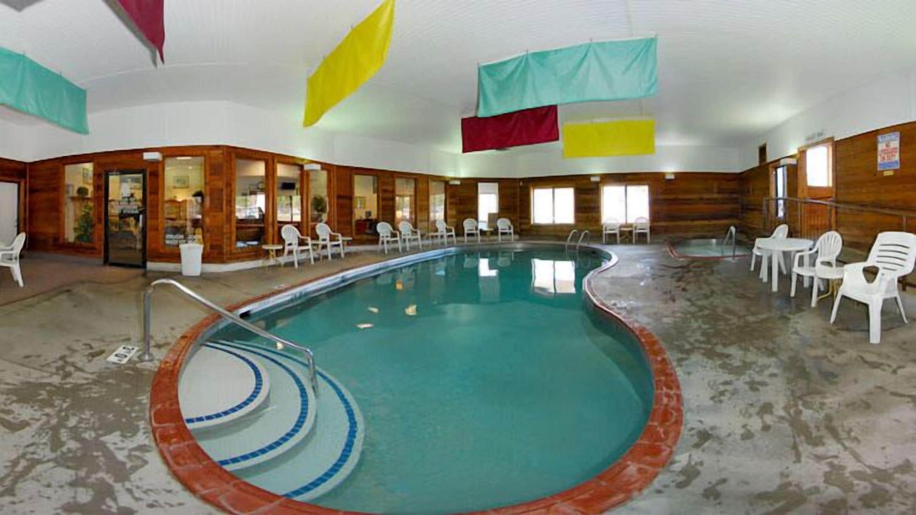 An indoor swimming pool with a tiled floor, surrounded by white plastic chairs and tables.
