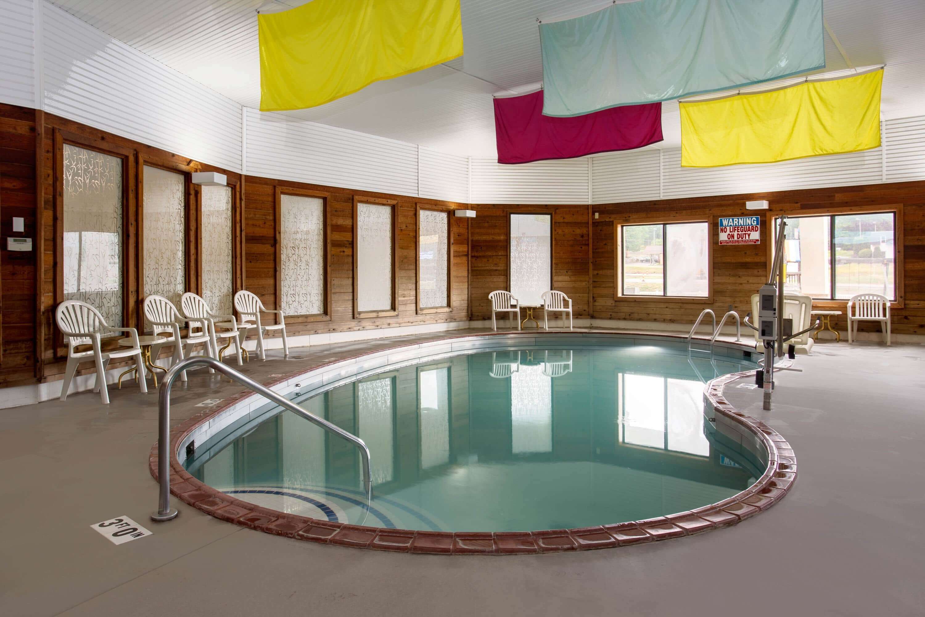 Una piscina interior con agua cristalina, rodeada de sillas blancas y una estación de socorrista.