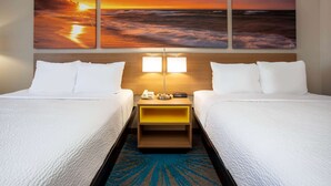 Ein Hotelzimmer mit zwei Betten, einem Nachttisch mit Lampe und einer Wand mit drei Sonnenuntergangsbildern.