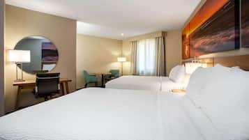 A hotel room with two beds, a desk, a chair, and a round mirror.
