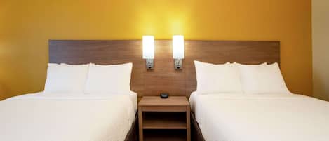 A hotel room with two beds, a wooden headboard, bedside lamps, and a red carpet.