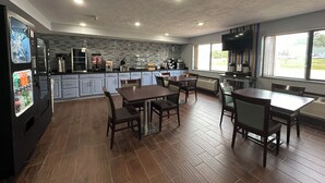 Een moderne keuken met grijze kastjes, een zwarte koelkast en een betegelde achterwand. In de eethoek staan houten tafels en stoelen.