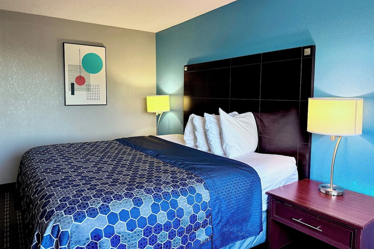 Quarto de hotel com uma cama grande, duas luminárias de cabeceira, uma mesa de apoio e uma obra de arte na parede.