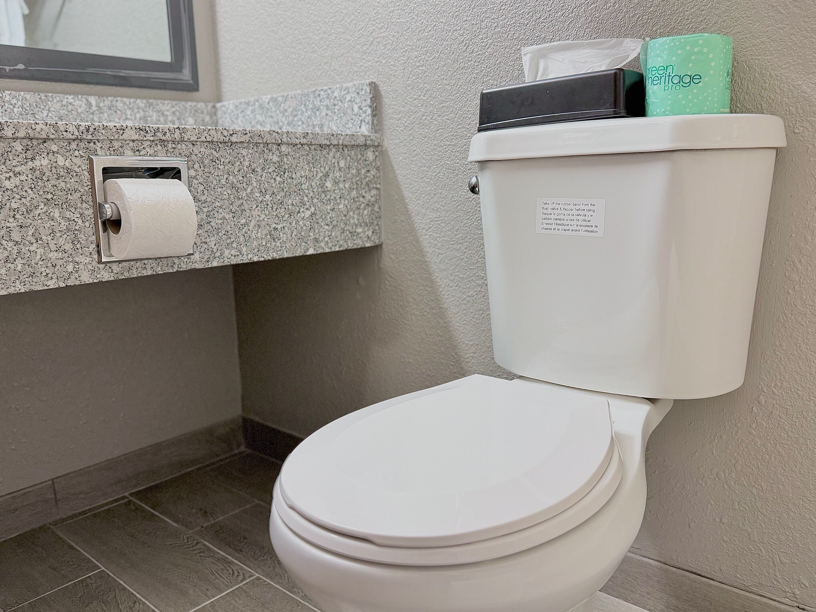 A white toilet with a paper towel holder and a green toilet paper roll on top.