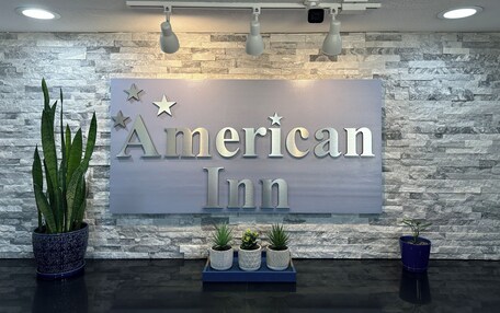 A reception area with a sign reading "American Inn," a stone wall, and potted plants.