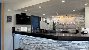 Een receptie met een stenen muur, een flatscreen televisie, een blauwe deur en een bord waarop 'American Inn' staat.