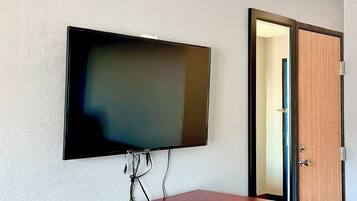 A room with a flat-screen TV mounted on the wall, a wooden door, and a small desk with a remote control.