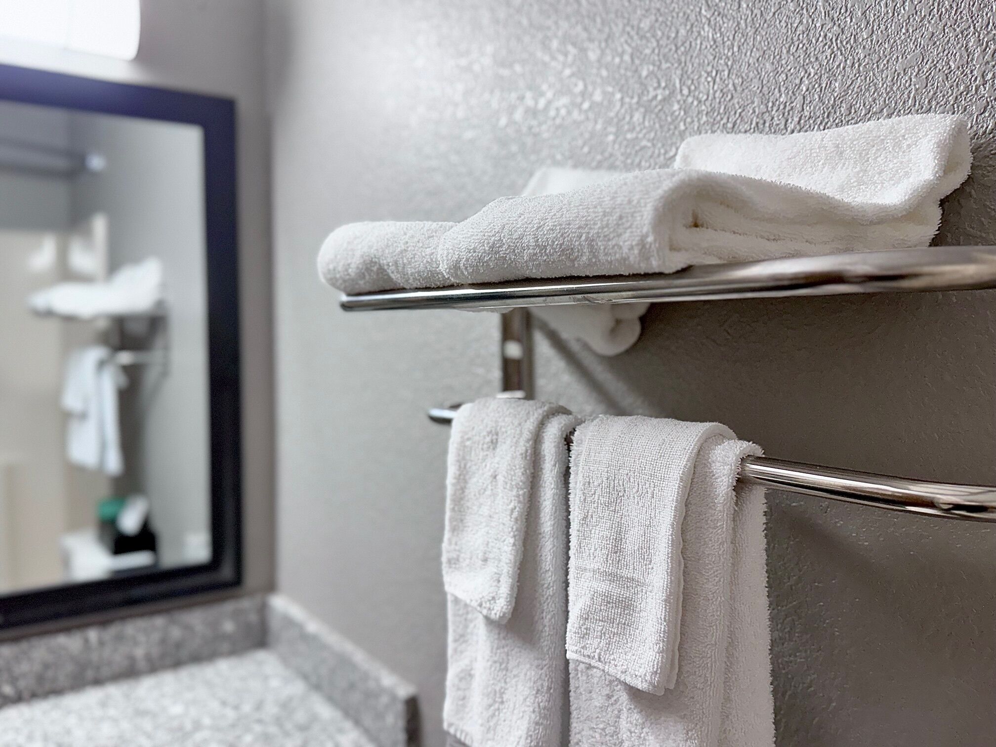A bathroom with a towel rack holding two folded towels and a mirror above it.