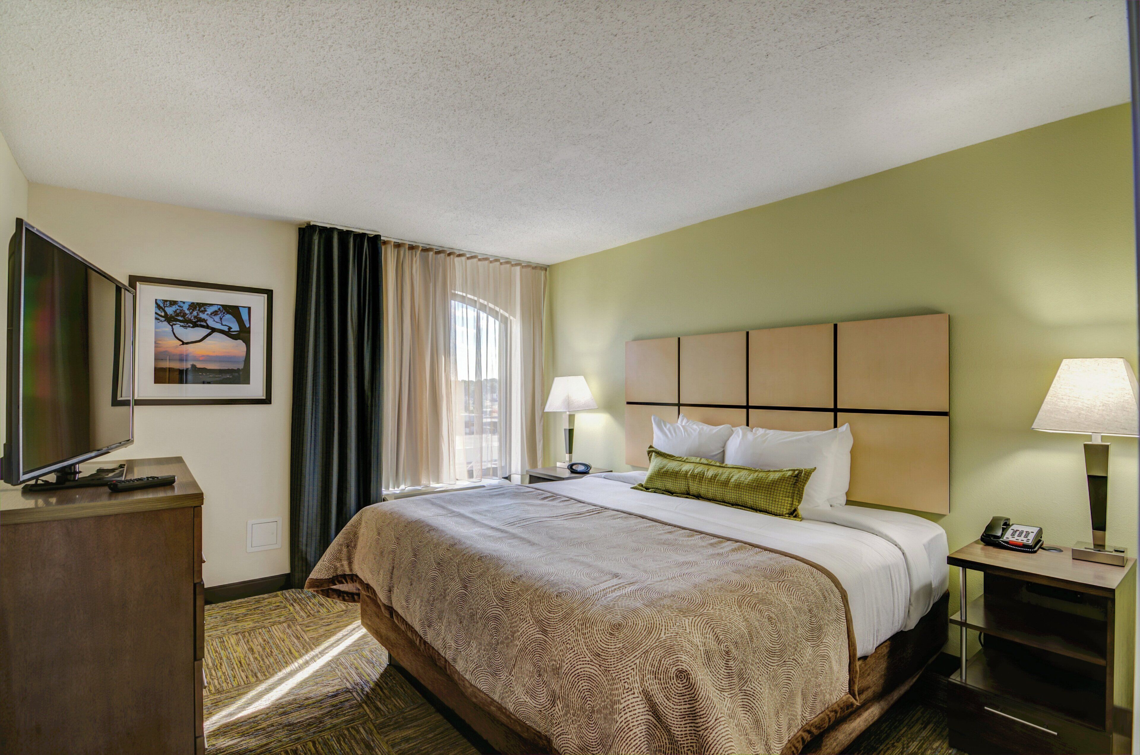 A hotel room with a bed, a desk, a television, a lamp, and a painting on the wall.