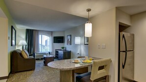 Une chambre d’hôtel compacte comprenant un coin cuisine, un espace repas, un canapé et une grande fenêtre.