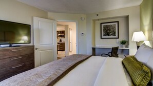 Une chambre d’hôtel équipée d’un lit, d’un bureau, d’une chaise, d’une télévision et d’une porte donnant sur un coin cuisine.
