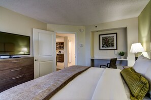 Ein Hotelzimmer mit Bett, Schreibtisch, Stuhl, Fernseher und einer Tür zu einer Küchenzeile.