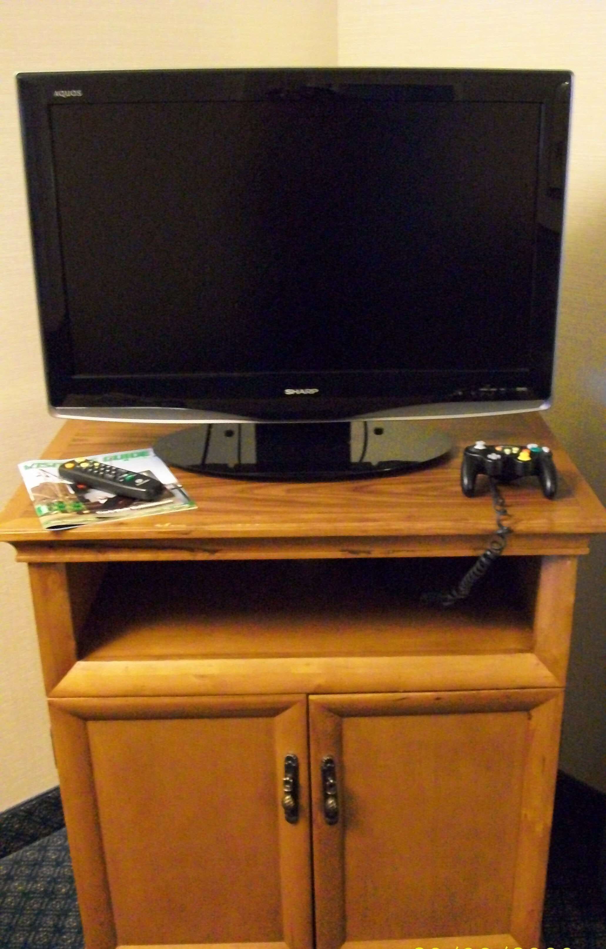 A television on a wooden stand with a remote control and a game controller on top.