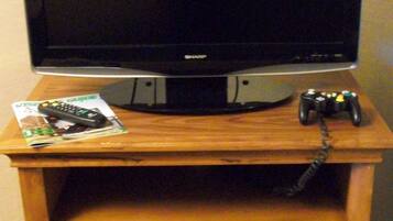 A television on a wooden stand with a remote control and a game controller on top.