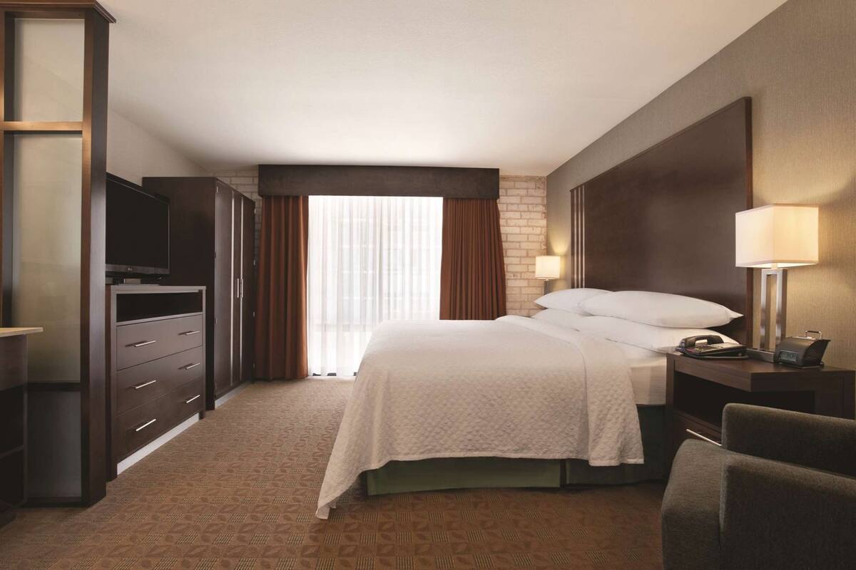 A hotel room with a bed, a TV, a desk with a lamp, and a chair.