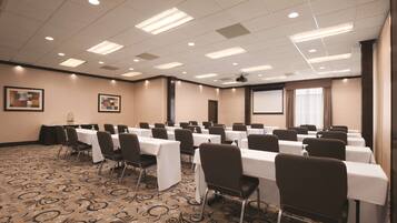 A conference room with tables and chairs, a projector screen, and a patterned carpet.