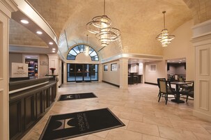 A spacious lobby with a high ceiling, modern chandeliers, and a reception desk.