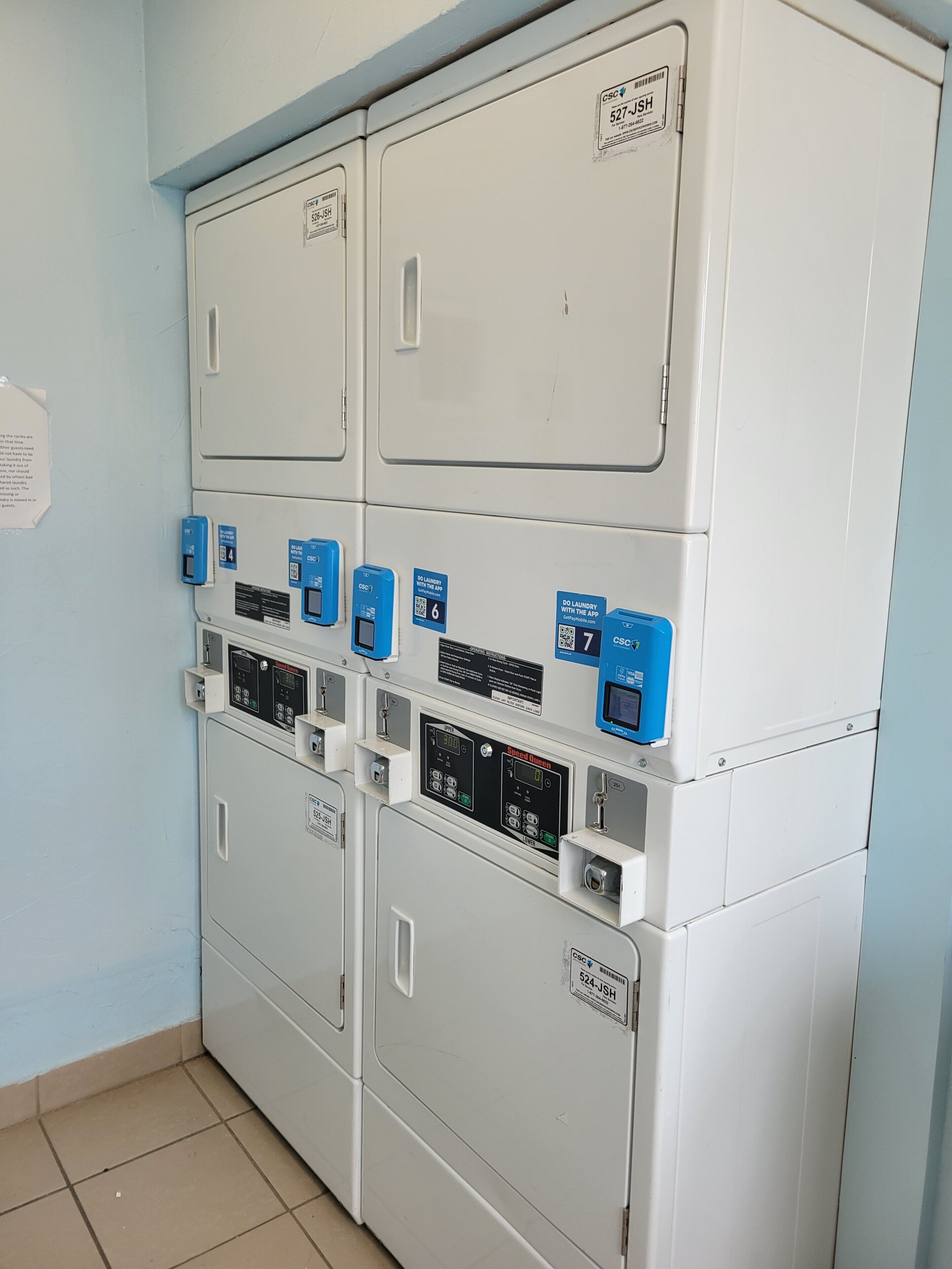 A laundry facility with multiple washing machines and dryers, control panels, and QR codes for digital services.