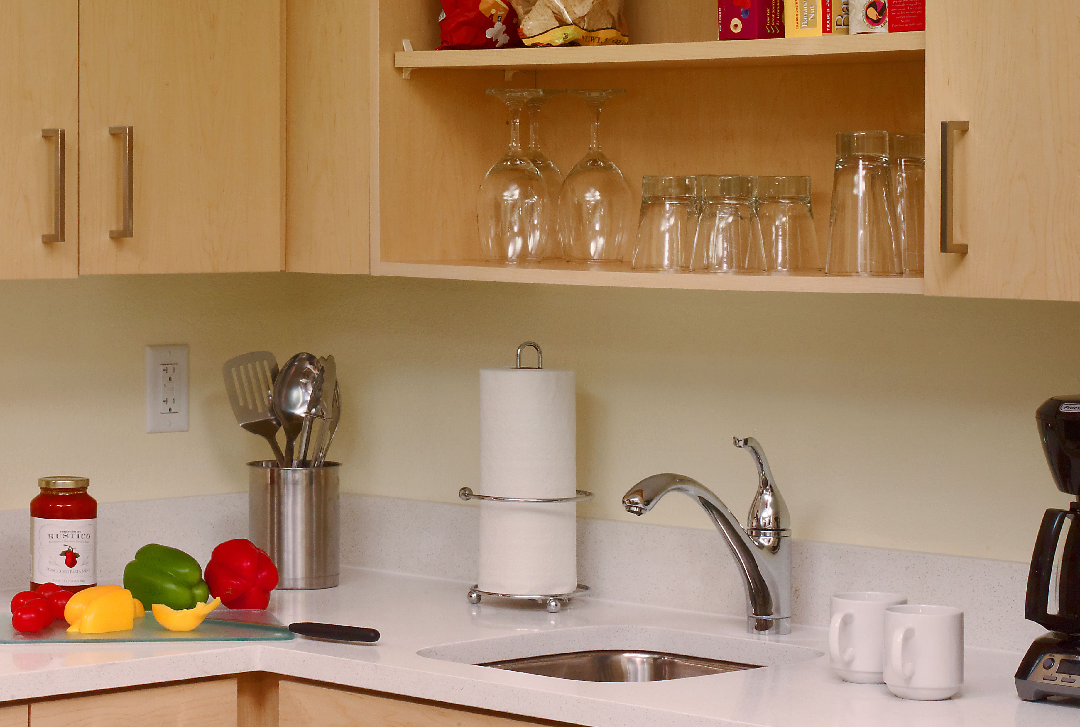 Een keuken met houten kastjes, een roestvrijstalen spoelbak en een aanrecht met diverse spullen, zoals een pot, bestek en een snijplank met groenten.