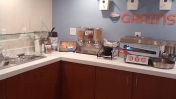 Una zona de cocina con mostrador, dispensadores de alimentos, una máquina de café y una pared con el letrero 'Grains'.